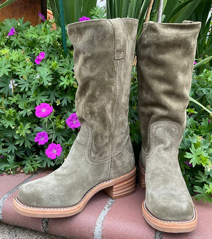 Frye green suede boots on a stone surface with plants and flowers in the background