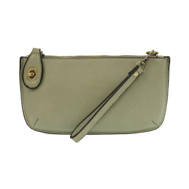 A barley mint-colored mini crossbody wristlet clutch with brass plated hardware and a printed lining, displayed with the wristlet strap visible