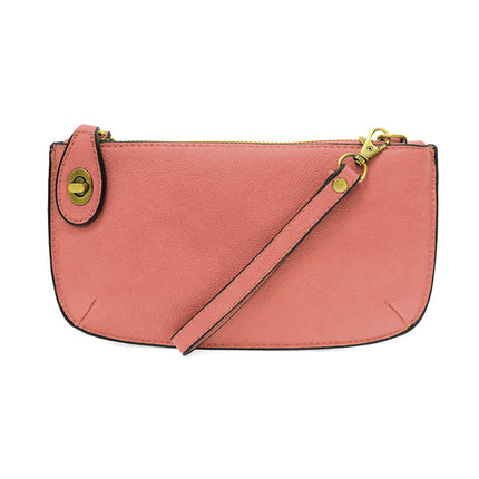 A blush-colored mini crossbody wristlet clutch with brass plated hardware and a printed lining, displayed with the wristlet strap visible