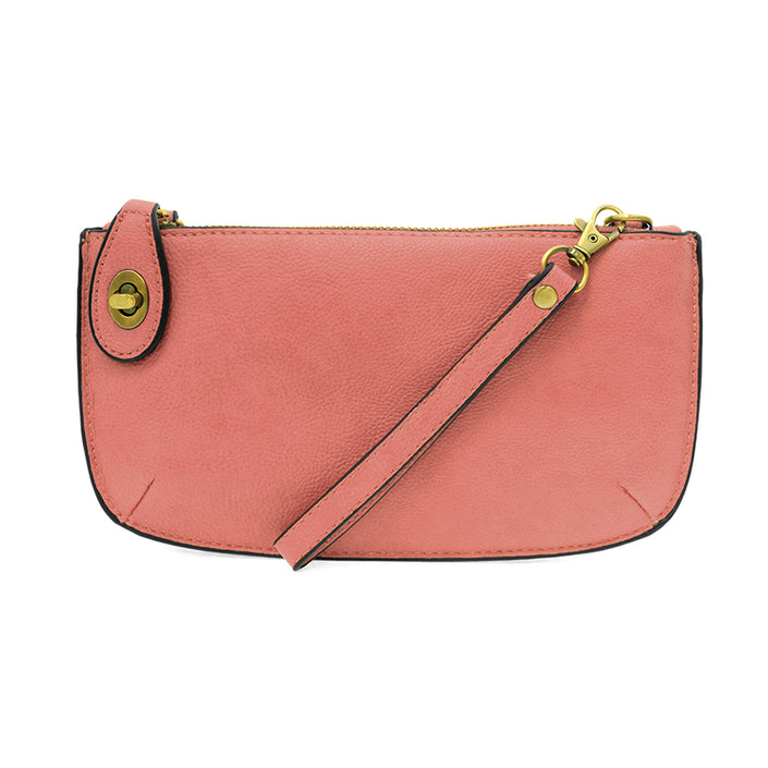 A blush-colored mini crossbody wristlet clutch with brass plated hardware and a printed lining, displayed with the wristlet strap visible