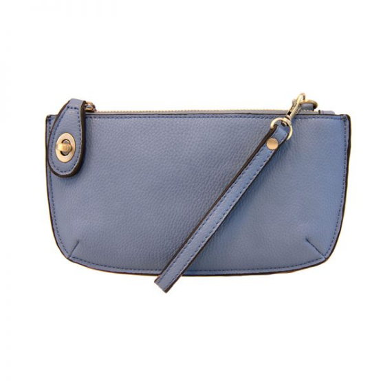 A chambray-colored mini crossbody wristlet clutch with brass plated hardware and a printed lining, displayed with the wristlet strap visible