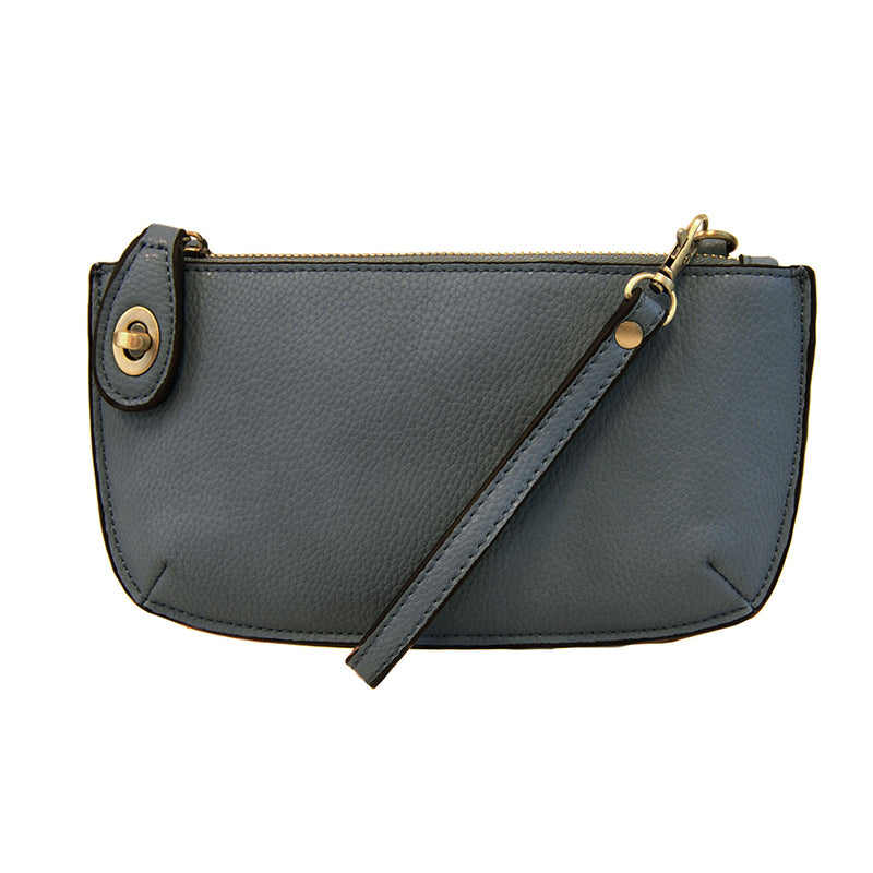 A dark chambray-colored mini crossbody wristlet clutch with brass plated hardware and a printed lining, displayed with the wristlet strap visible