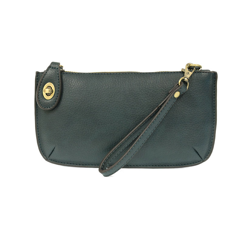 A dark teal-colored mini crossbody wristlet clutch with brass plated hardware and a printed lining, displayed with the wristlet strap visible