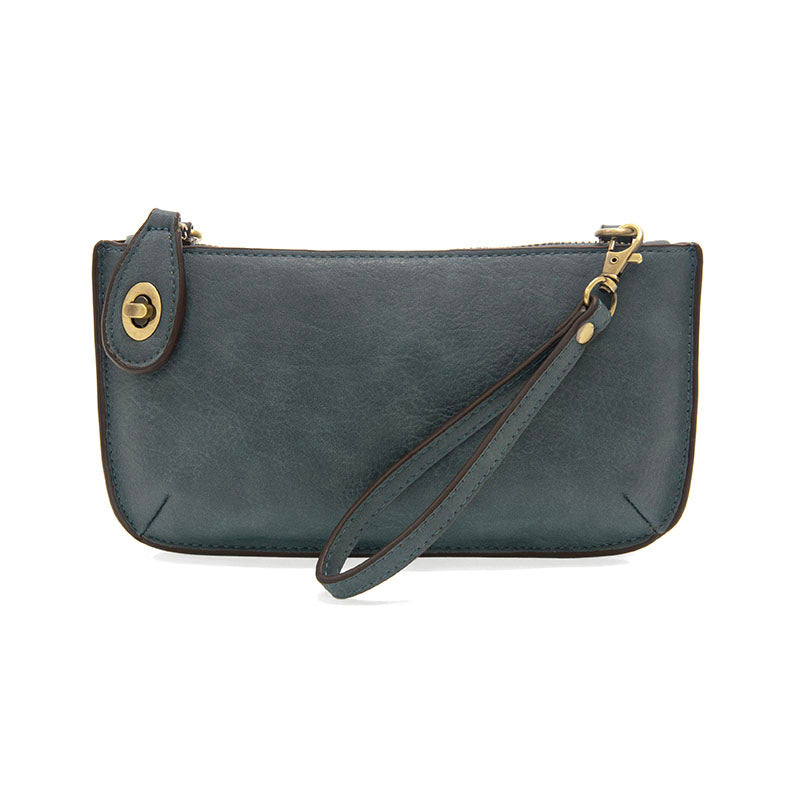 A denim-colored mini crossbody wristlet clutch with brass plated hardware and a printed lining, displayed with the wristlet strap visible