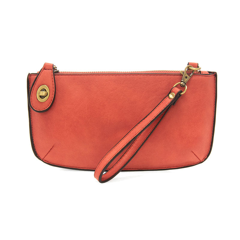 A desert coral-colored mini crossbody wristlet clutch with brass plated hardware and a printed lining, displayed with the wristlet strap visible