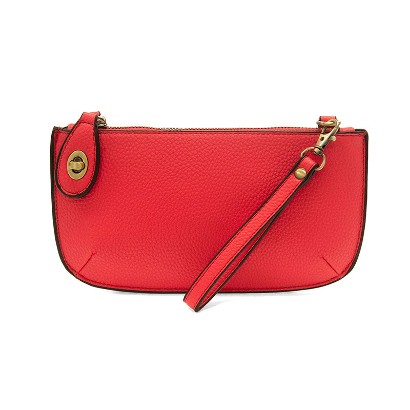An extreme rose-colored mini crossbody wristlet clutch with brass plated hardware and a printed lining, displayed with the wristlet strap visible