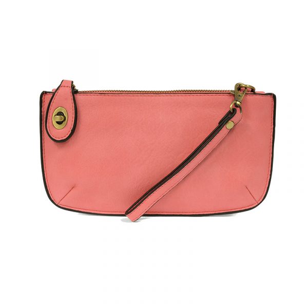 A pink-colored mini crossbody wristlet clutch with brass plated hardware and a printed lining, displayed with the wristlet strap visible