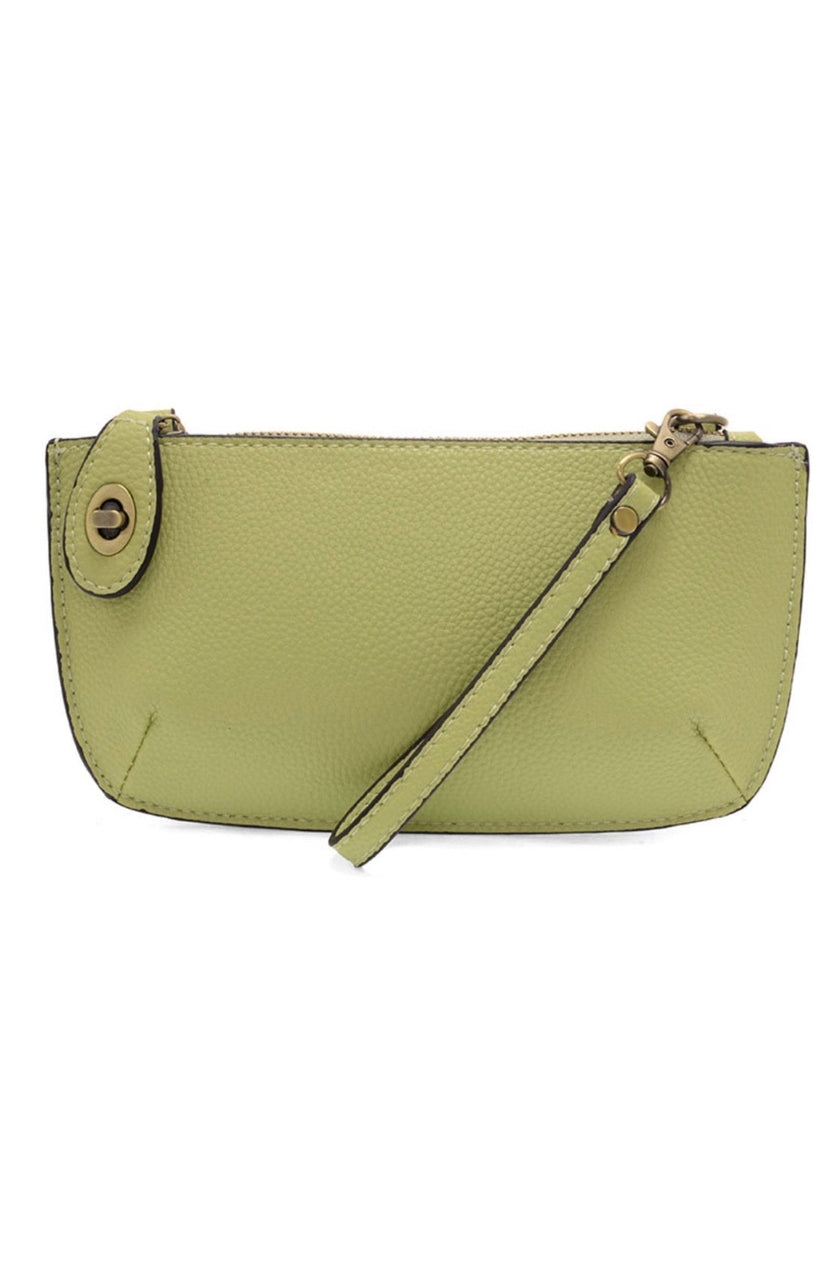 A kiwi-colored mini crossbody wristlet clutch with brass plated hardware and a printed lining, displayed with the wristlet strap visible