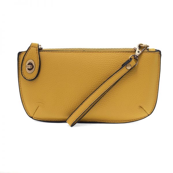 A mustard-colored mini crossbody wristlet clutch with brass plated hardware and a printed lining, displayed with the wristlet strap visible