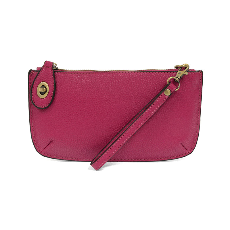 A fuchshia-colored mini crossbody wristlet clutch with brass plated hardware and a printed lining, displayed with the wristlet strap visible