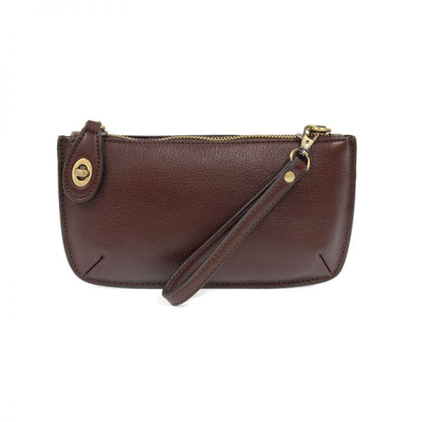 An oxblood-colored mini crossbody wristlet clutch with brass plated hardware and a printed lining, displayed with the wristlet strap visible