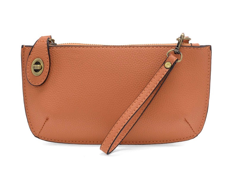 A peach-colored mini crossbody wristlet clutch with brass plated hardware and a printed lining, displayed with the wristlet strap visible