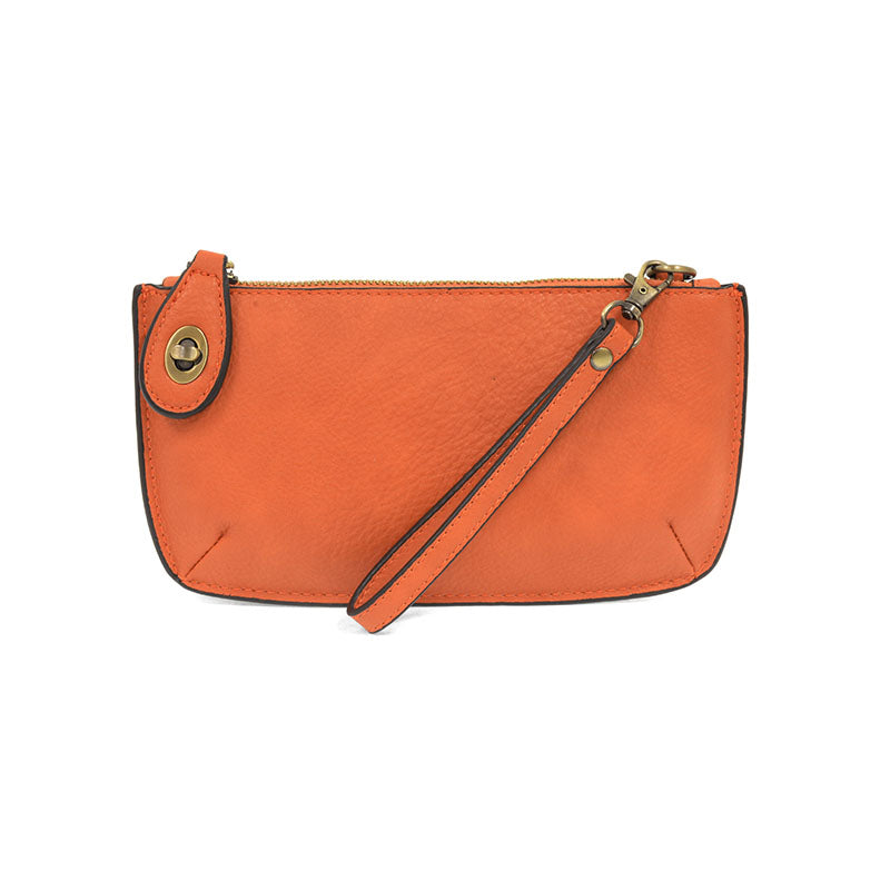 A pumpkin-colored mini crossbody wristlet clutch with brass plated hardware and a printed lining, displayed with the wristlet strap visible