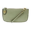 A sage-colored mini crossbody wristlet clutch with brass plated hardware and a printed lining, displayed with the wristlet strap visible