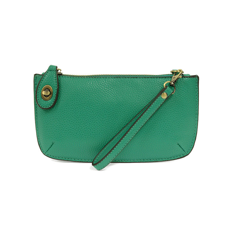 A tropical green-colored mini crossbody wristlet clutch with brass plated hardware and a printed lining, displayed with the wristlet strap visible
