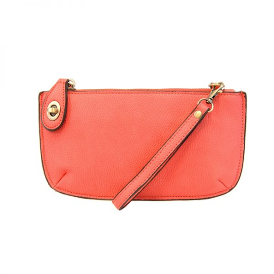 A watermelon-colored mini crossbody wristlet clutch with brass plated hardware and a printed lining, displayed with the wristlet strap visible