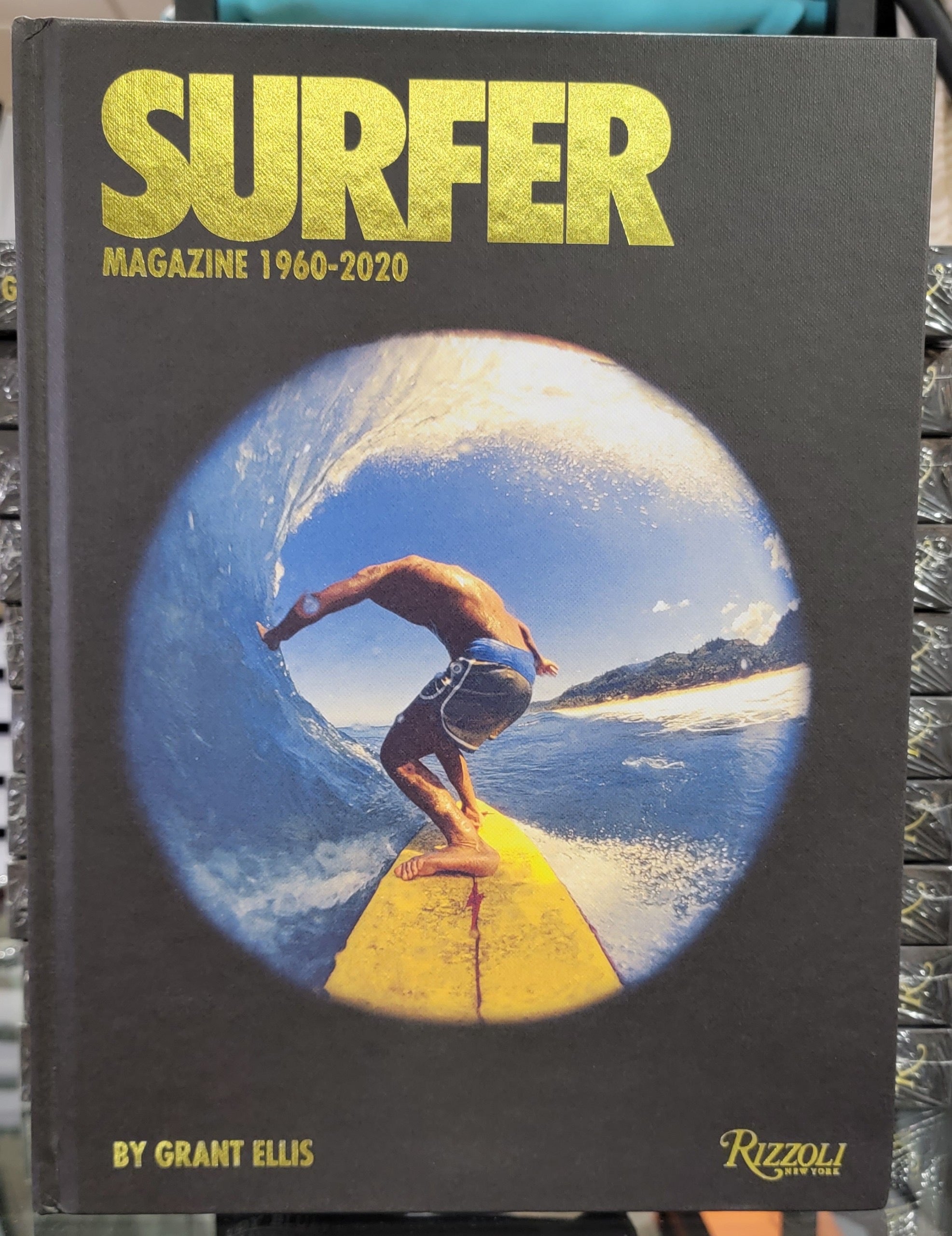 The cover of Surfer Magazine 1960-2020 features a striking fisheye photo of a surfer riding a wave from the back of a yellow surfboard, with the title 