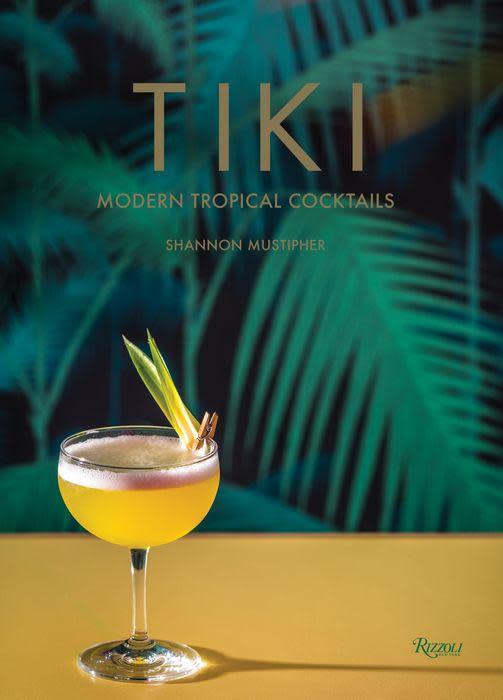 A yellow tropical cocktail made with Caribbean rums sits on a yellow surface in front of the book 